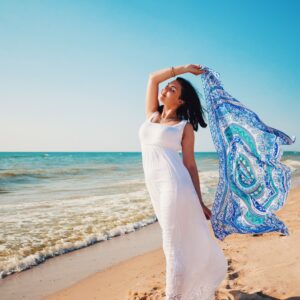 Portrait of beautiful woman in white dress and mandala silk scarf in hand walking on beach near sea